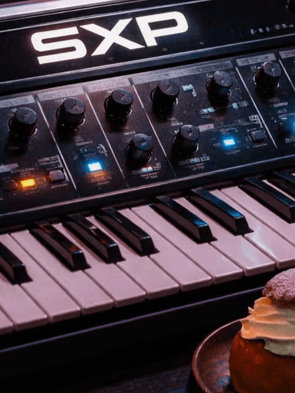 Synthesizer with Standard X Project logo on it, swedish semla and coffee standing infront of it
